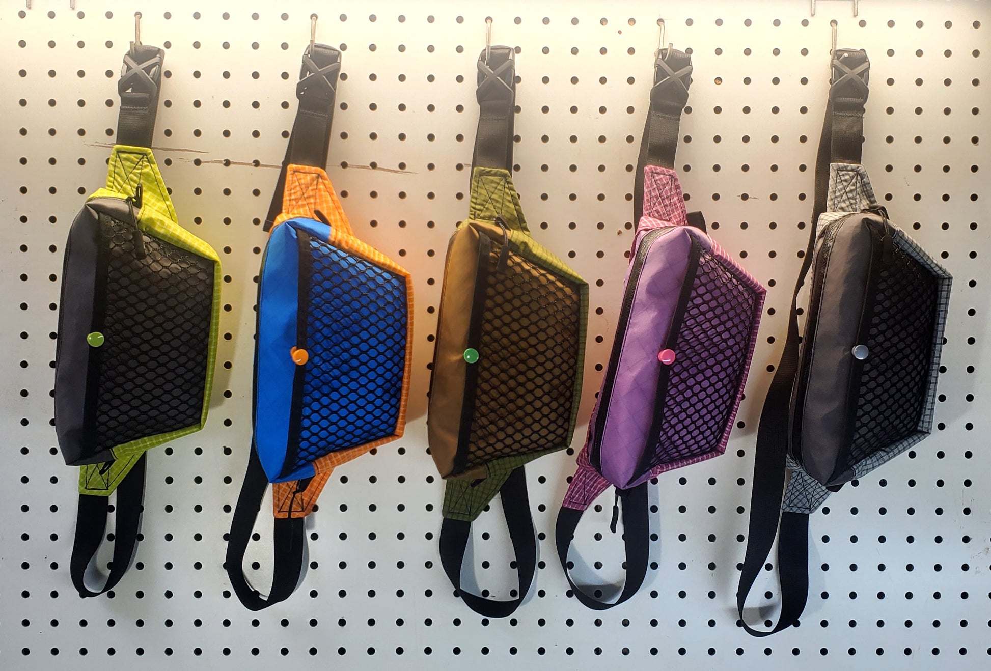 UL fanny packs in multiple color schemes hanging on peg board wall
